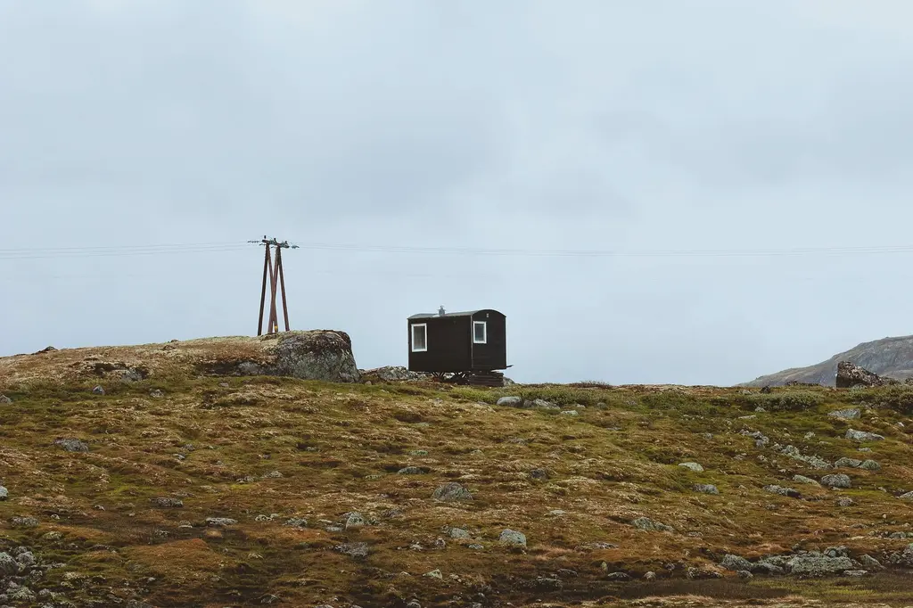 A small dark hut on a low rise of moss and rock under a wide pale grey sky.