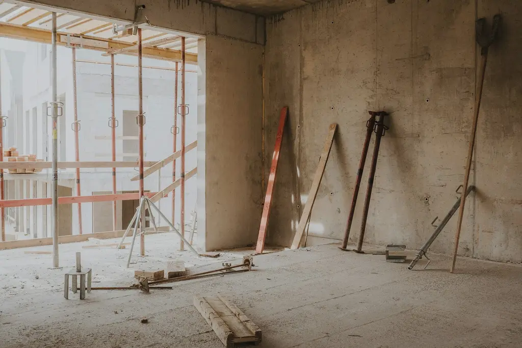 The inside of a concrete warehouse during works, with steel props and scaffolding in front of a tall opening and tools leaning against a rough wall.