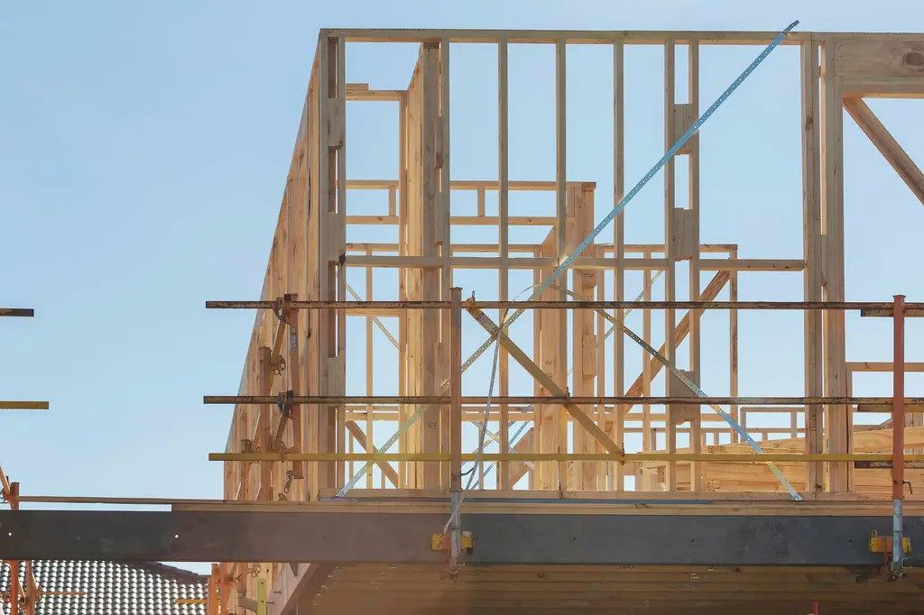A tall timber stud frame with horizontal bracing and a steel beam, standing against a pale blue sky.