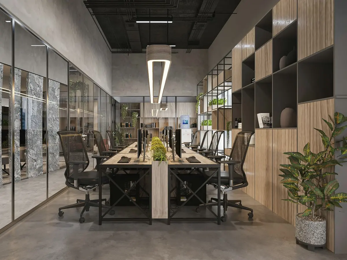 A long open studio with a row of desks, black office chairs, glass partitions, a timber shelf wall and a suspended linear lamp.