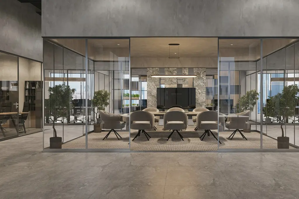 A glass-walled meeting room with a long table and round-backed chairs, set inside a large concrete hall with a stone feature wall behind.